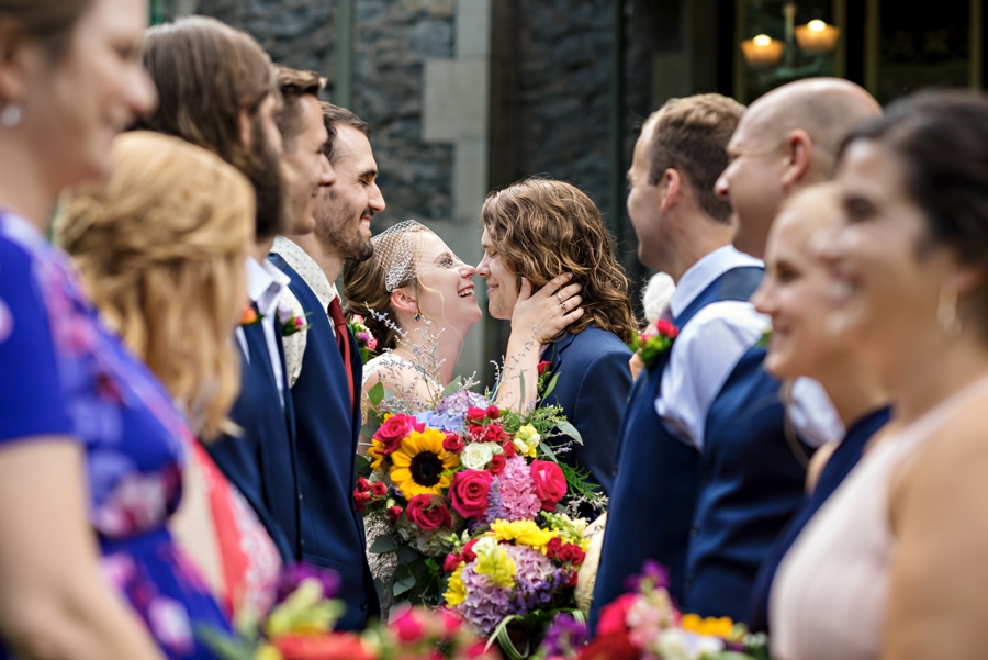 A newly married bride and groom kiss while surrounded by their bridal party.